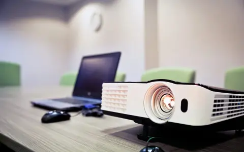 Rzutnik i laptop na stole, gotowe do prezentacji. Dowiedz się, jak podłączyć rzutnik do laptopa, by rozpocząć pokaz.