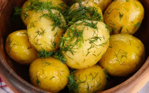 Ziemniaki gotowane w drewnianej misce, posypane świeżym koperkiem. Aromatyczne i apetyczne danie.