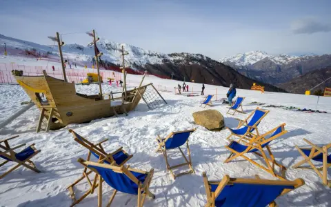 Alpe di Mera: un galeone di legno e sdraio blu attendono i visitatori sulla neve, con montagne innevate sullo sfondo.