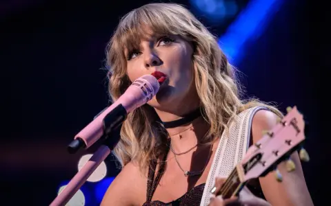 Taylor Swift śpiewa do różowego mikrofonu, grając na gitarze. To scena z jej epickiej trasy "reputation stadium tour", która na zawsze zmieniła jej wizerunek.