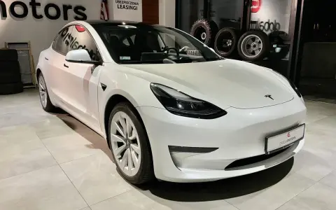 Biała Tesla Model 3 z napędem na cztery koła stoi w salonie samochodowym.