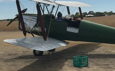 Grüner Doppeldecker, bereit zum Start. Ein Pilot und ein Passagier sitzen im Cockpit. Das Flugzeug erinnert an einen Tiger Moth.