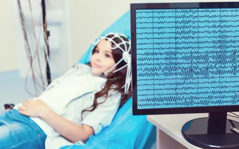 Dziewczynka z czepkiem EEG leży na kozetce, a na monitorze widać zapis fal mózgowych. Badanie pomaga zrozumieć zespół Aspergera a wynik EEG.