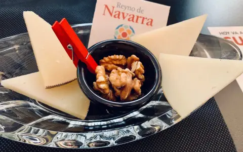 Queso en cuñas con nueces en un cuenco negro, sobre plato de cristal y tarjeta "Reino de Navarra".