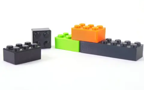 Klocki z drukarki 3D, wykonane z materiału ABS, w kolorach czarnym, zielonym i pomarańczowym, ułożone na białym tle.