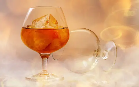 Ein Glas mit bernsteinfarbenem Brandy und Eiswürfeln steht neben einem leeren, umgekippten Glas. Was ist ein Brandy? Ein edles Getränk.