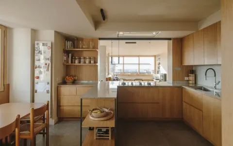 Cocinas color madera con encimeras de granito, electrodomésticos integrados y una isla central. Un comedor adyacente con mesa y sillas de madera.