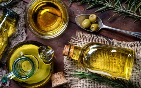 Aceite de oliva en botellas y cuenco, con aceitunas y romero. A pesar de sus beneficios, hay desventajas del aceite de oliva, como su precio.