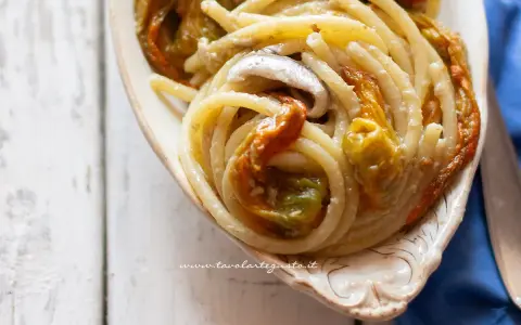 Un piatto di pasta con fiori di zucca cremosa, condita con acciughe e servita in una ciotola decorata.