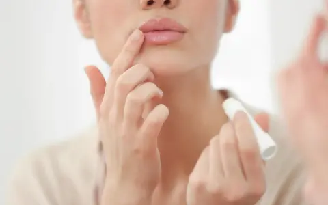 Una mujer aplica bálsamo labial, mostrando cómo son los labios perfectos: hidratados y suaves.
