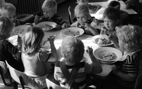 Kinder essen gemeinsam Brei. Ein Junge isst genüsslich, ein anderes Kind schaut nachdenklich. Erinnerungen an Kindheits Eis.