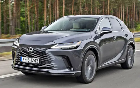 Szary Lexus RX 2026 jedzie po drodze, las w tle.