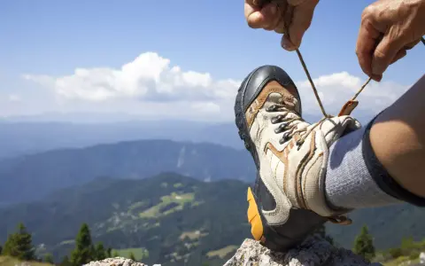 Ręka zawiązuje sznurówki buta trekkingowego na tle górskiego krajobrazu. Właściwe wiązanie butów to klucz do komfortowej wędrówki.