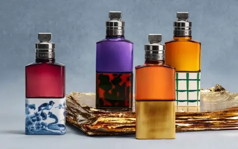 Vier bunte Parfumflaschen mit silbernen Verschlüssen auf goldenem Untergrund.