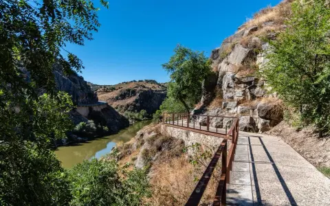 Sendero con barandilla de metal junto a un río y rocas, ideal para rutas senderismo Toledo.
