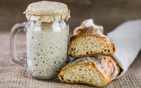 Un bocal de levain actif, prêt à être utilisé pour entretenir son levain, à côté de deux belles tranches de pain artisanal.