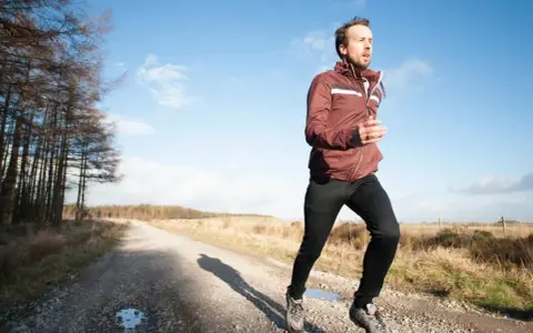 Mann joggt bei 10 Grad in einer leichten Jacke und Hose auf einem Feldweg.