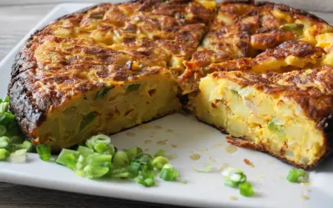 Pyszna tortilla de patatas, pokrojona na kawałki, z zieloną cebulką na talerzu.