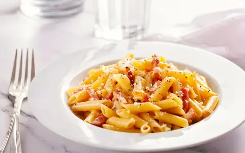Piatto di pasta penne con speck e zafferano, guarnito con parmigiano e pepe nero.