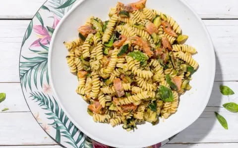 Un piatto invitante di pasta fredda con zucchine e salmone, condita con basilico fresco. Perfetta per un pasto estivo leggero e gustoso.