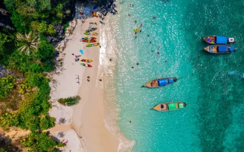 Rajska plaża na tajlandzkiej wyspie Phuket. Kajaki czekają na plaży, a turyści kąpią się w turkusowej wodzie.