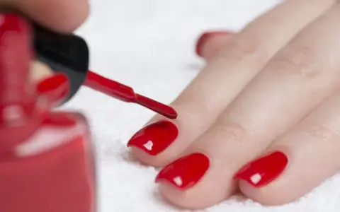 Dopo il primer unghie, si applica lo smalto rosso brillante. La mano è pronta per la manicure.