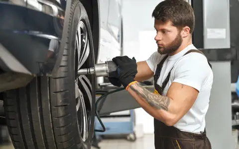 Mechanik z tatuażem dokręca śrubę koła. Zwróć uwagę na objawy zużycia sworznia wahacza, gdy słyszysz stuki.