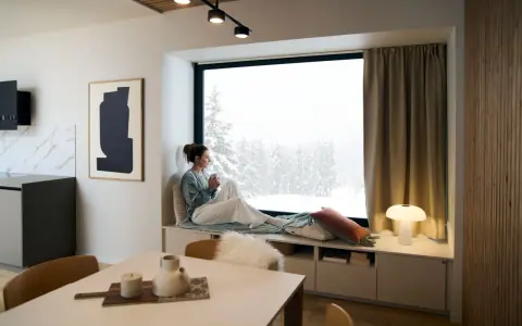 Femme savourant une boisson chaude dans un coin lecture cocooning, regardant la neige tomber.