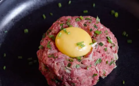 Delicioso steak tartar de wagyu con yema de huevo y cebollino picado, servido en un plato negro.
