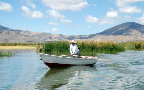 Donna con cappello di paglia rema su un lago, con montagne sullo sfondo. Mete agosto fuori Europa, un'immagine di pace.