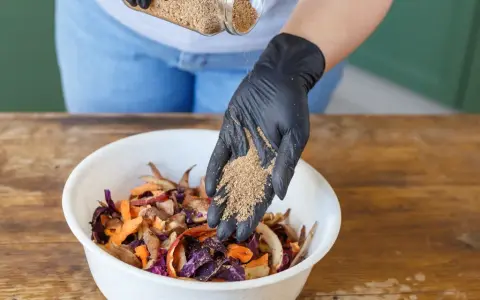 Ajout de bran de riz pour le bokashi maison. Des restes de légumes colorés attendent dans un bol blanc.