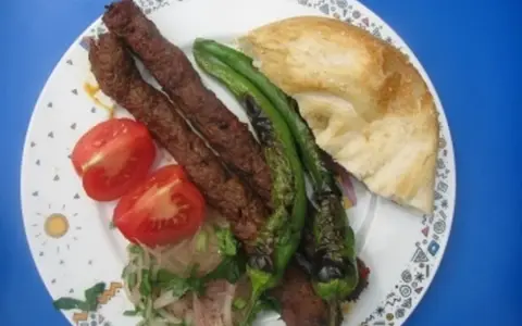 Adana Kebap mit gegrillten Peperoni, Tomaten und Fladenbrot auf einem Teller.