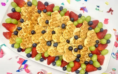Herzförmige Waffeln mit Erdbeeren, Blaubeeren und grünen Trauben auf einem Teller – ein bunter obstteller kinder für jeden Anlass.