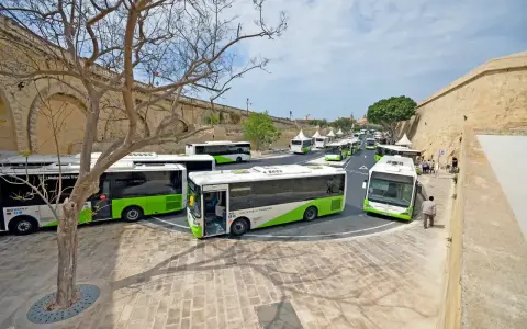 Kolejka zielono-białych autobusów Malta Public Transport czeka na pasażerów. Lotnisko na Malcie tętni życiem.