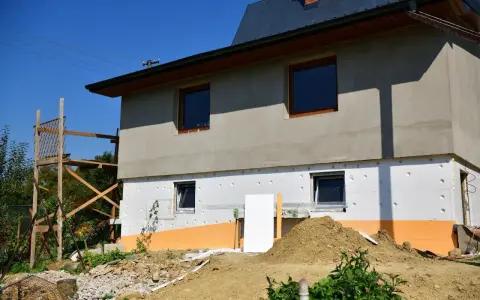 Budynek w trakcie ocieplania styropianem. Widoczne okna, rusztowanie i ziemia. Trzeba uważać na **mostek termiczny** przy oknach.