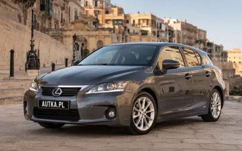 Szary Lexus CT 200h zaparkowany na brukowanej uliczce z zabytkowymi budynkami w tle.