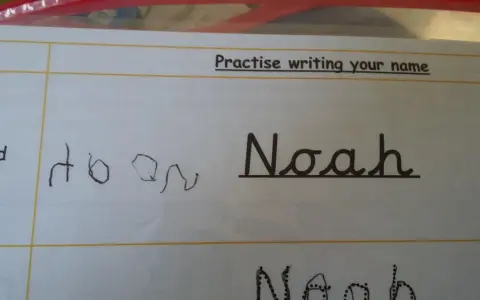 Siedmiolatek ćwiczy pisanie imienia "Noah" w lustrzanym odbiciu. Obok widać próbę pisania imienia.