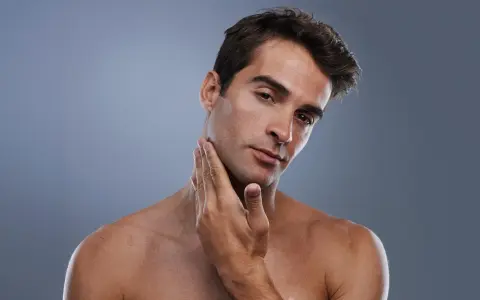 Hombre joven con piel suave y un afeitado perfecto, tocando su mandíbula con la mano.