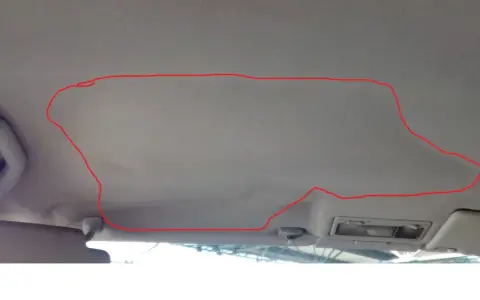 Opadająca podsufitka w samochodzie, zaznaczona czerwoną linią. Rozwiązaniem może być naprawa podsufitki pinezkami.