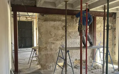 Trabajador realiza el empresillado de pilares en una obra. Se aprecian puntales metálicos y vigas de soporte.