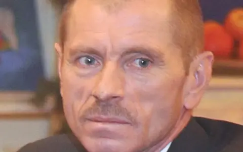 Portret Stanisława Pąka. Mężczyzna z wąsikiem patrzy w bok. W tle owoce.