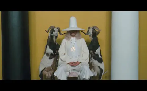 Uomo con cappello conico bianco e due capre imbalsamate, simbolo de la montagna sacra Jodorowsky.