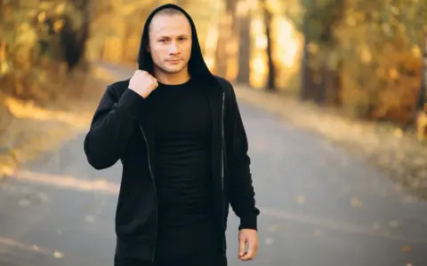 Mężczyzna w czarnej bluzie męskiej Guess z kapturem, stojący na ścieżce w jesiennym parku.