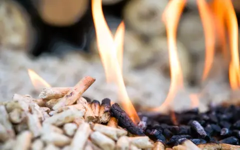 Fiamme danzano su pellet in combustione, un primo piano che mostra il passaggio dal legno chiaro alla cenere scura.