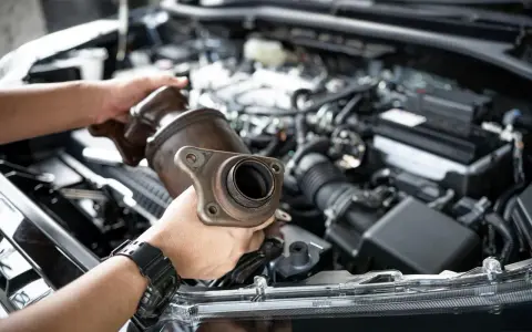Mechanic holding a catalytic converter, ready for replacement. Understanding the catalytic converter replacement cost is key for car owners.