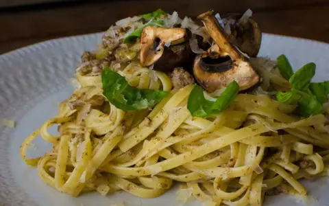 Pasta con champiñones, carne picada y queso rallado, decorada con hojas verdes.