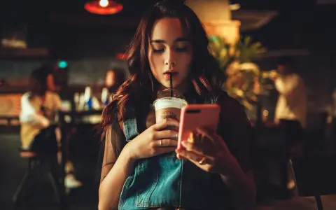 Dziewczyna popija kawę, przeglądając telefon. Może właśnie czyta, że jej facet przestał się odzywać z dnia na dzień.