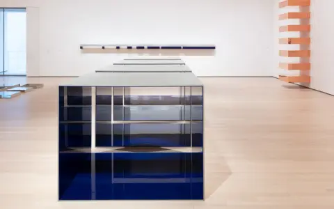 Installazione di Donald Judd con elementi blu e metallici su pavimento in legno chiaro, in una galleria d'arte.