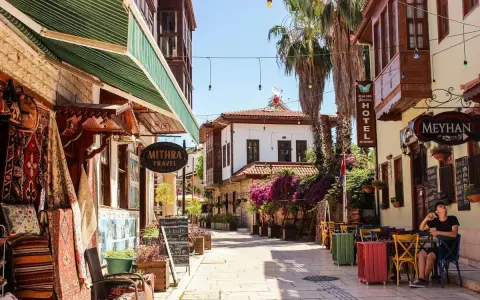 Bunte Gassen in der antalya altstadt mit Teppichläden, Palmen und einem Café, wo ein Mann entspannt sitzt.