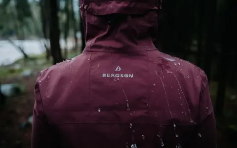 Krople deszczu spływają po bordowej kurtce przeciwdeszczowej Bergson. Idealna na wędrówki w deszczową pogodę.